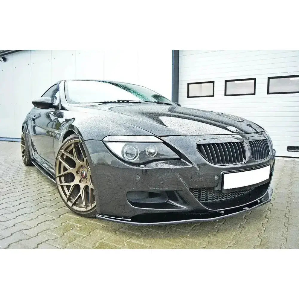Frontspoiler på svart Bmw M6 E63 med bronsefargede felger og regndråper foran garasjeport.