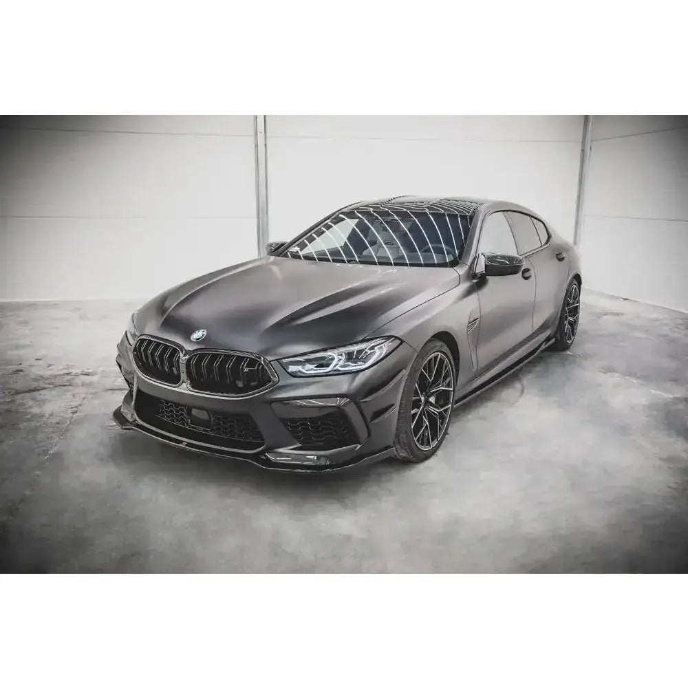 Frontsplitter på matt sort BMW M8 Gran Coupe F93 med store felger og markante luftinntak i lyst rom.