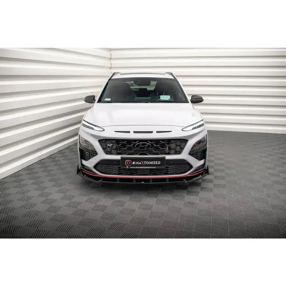 Front lip på Hyundai Kona N Mk1 med røde detaljer og sort grill, sett forfra i lyst rom.