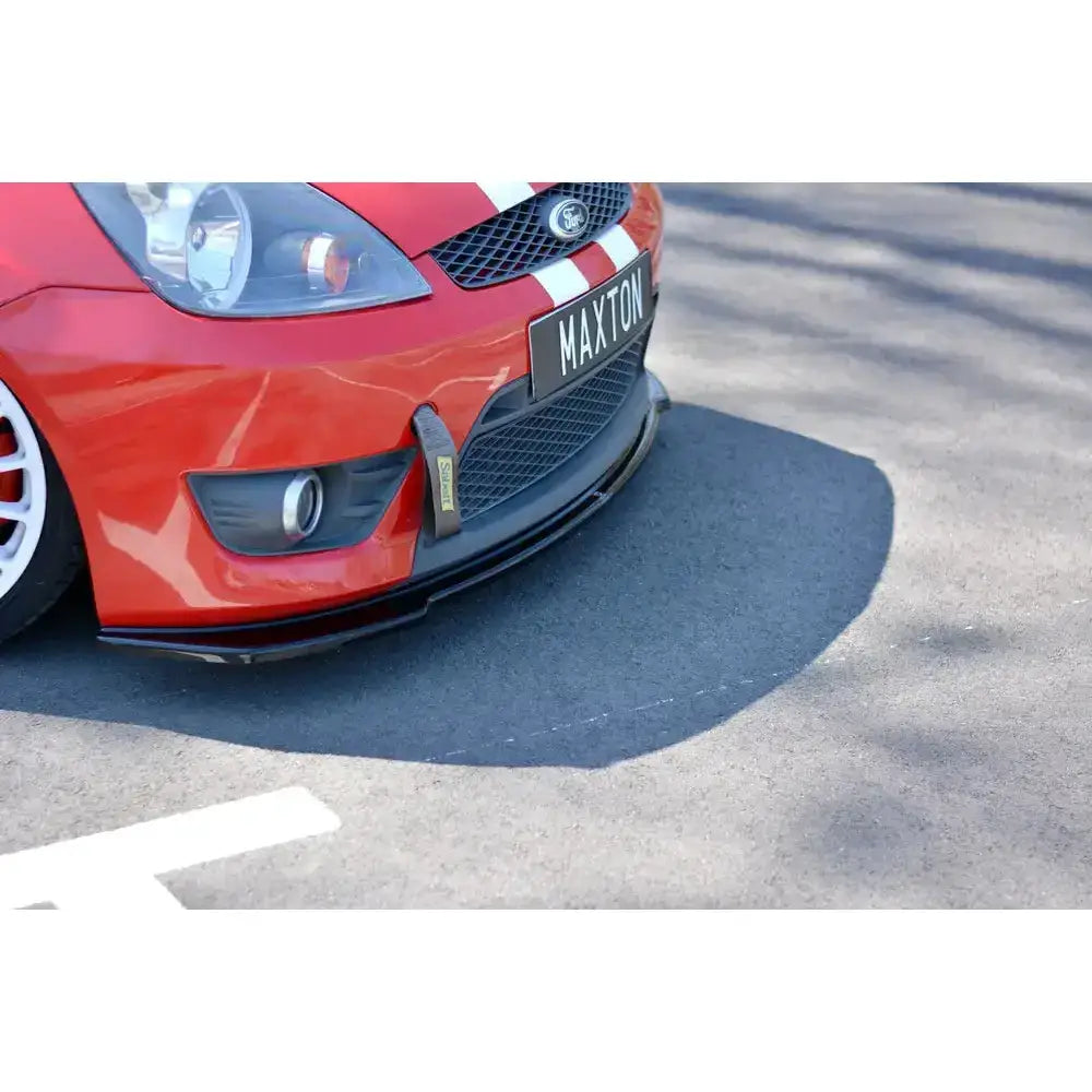 Front lip på Ford Fiesta Mk6 ST med sort frontsplitter, røde karosseri og hvite striper, parkert på asfalt.