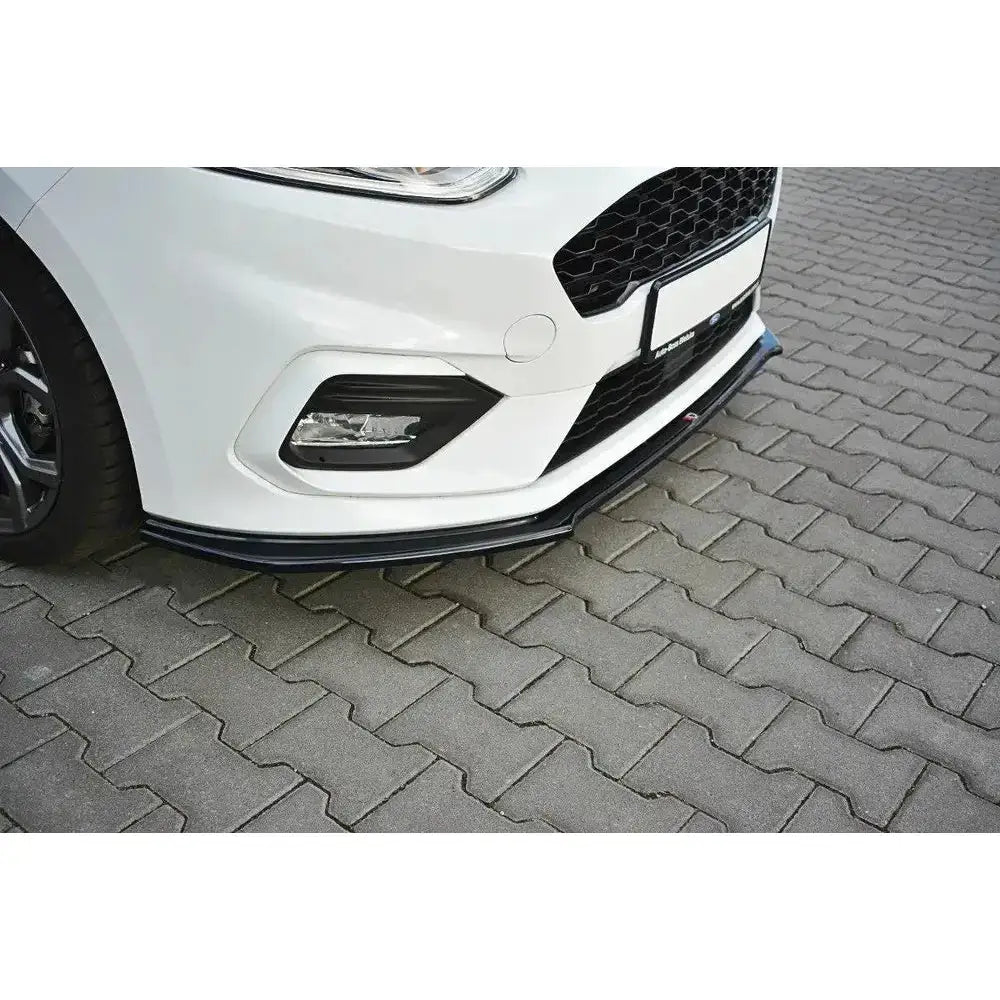 Frontsplitter til Ford Fiesta Mk8 ST-Line, sort, montert på hvit bil, sett fra siden på brostein.