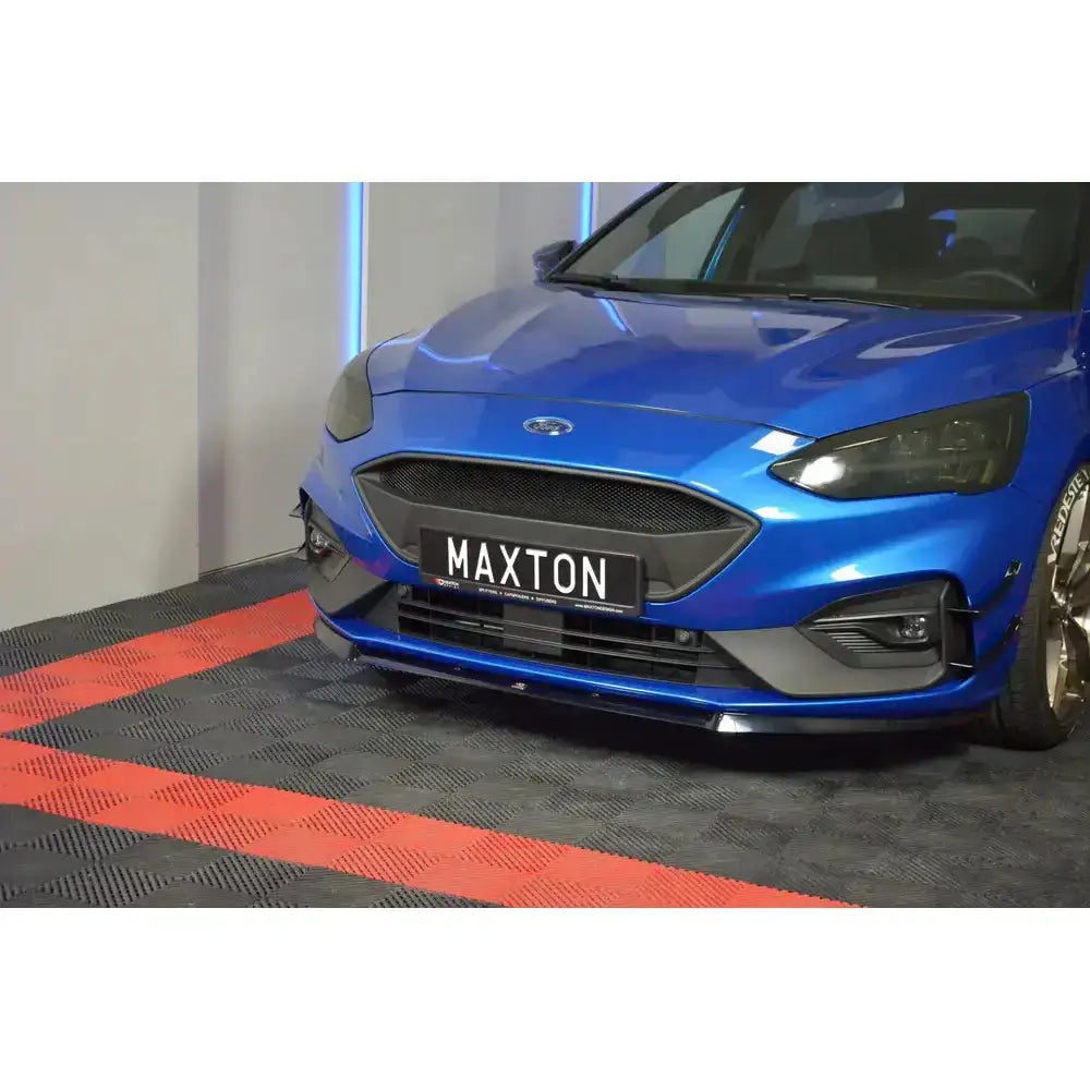 Frontspoiler på blå Ford Focus ST MK4 med sort grill og sporty detaljer, parkert på rutete gulv.
