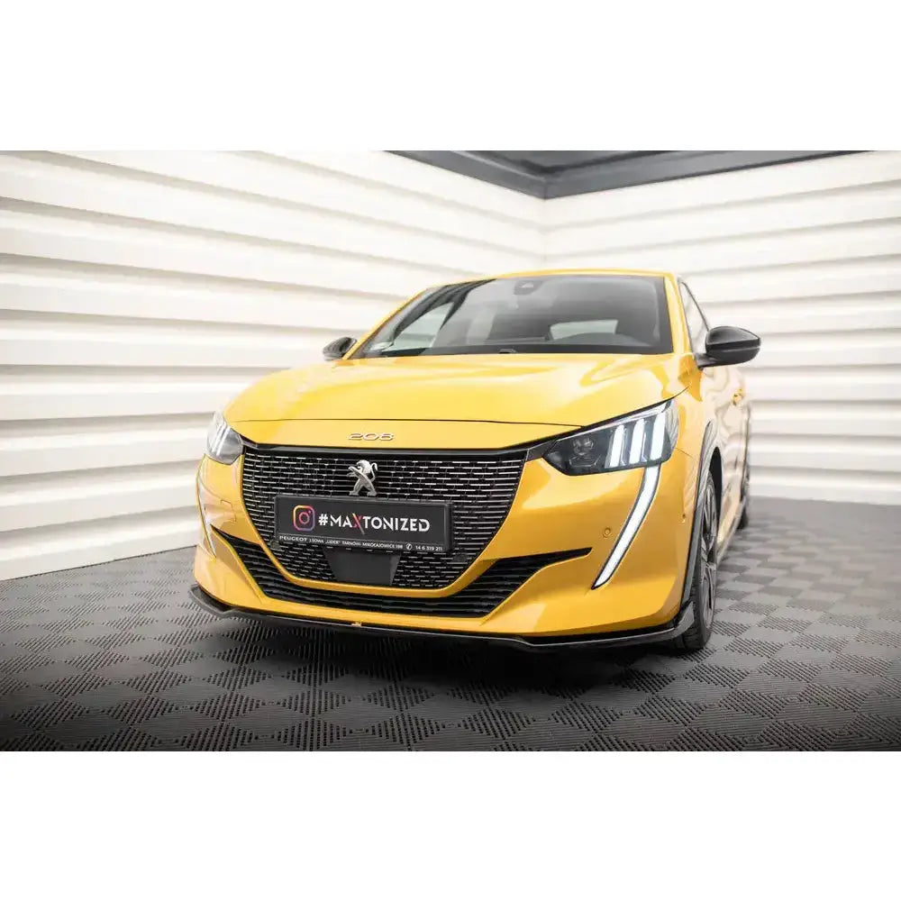 Front lip på Peugeot 208 GT Mk2 i gul med stor sort grill og markante LED-lys, innendørs på svart gulv.