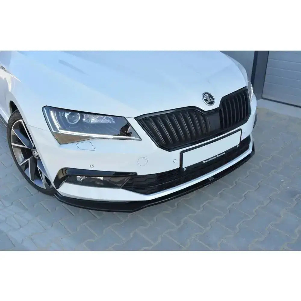 Frontsplitter på Skoda Superb III, nærbilde av hvit bil med sort grill og svart frontleppe på belegningsstein.