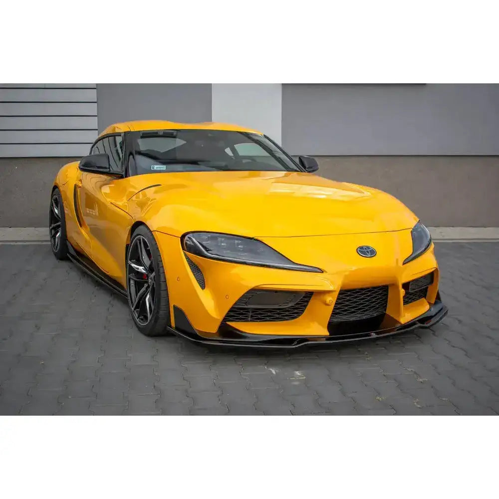 Frontspoiler på gul Toyota Supra Mk5 med sorte detaljer og store felger, parkert på brostein.
