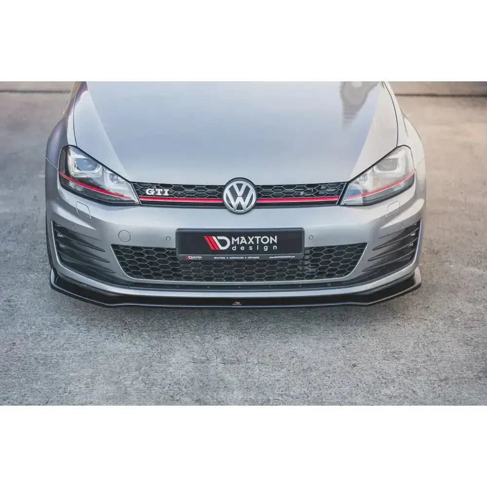 Frontspoiler på sølvfarget VW Golf VII GTI med sort frontsplitter, rød stripe i grillen og GTI-emblem.