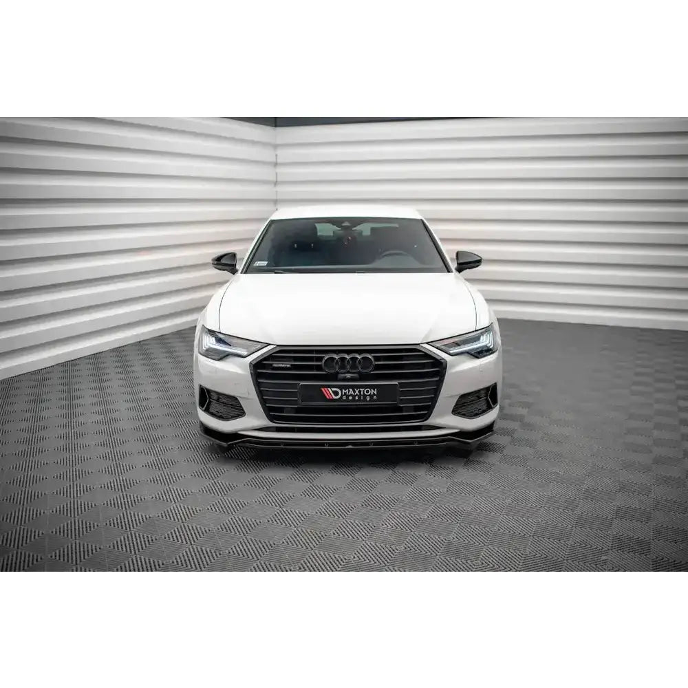 Front lip på hvit Audi A6 C8 sett forfra med mørk grill og Audi-ringer, innendørs på rutete gulv.