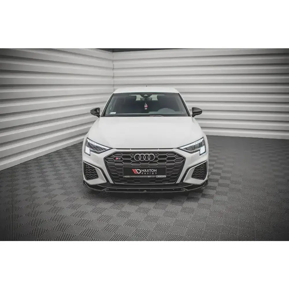 Frontspoiler på hvit Audi S3 med sort grill og LED-lys, avbildet rett forfra i lyst rom.