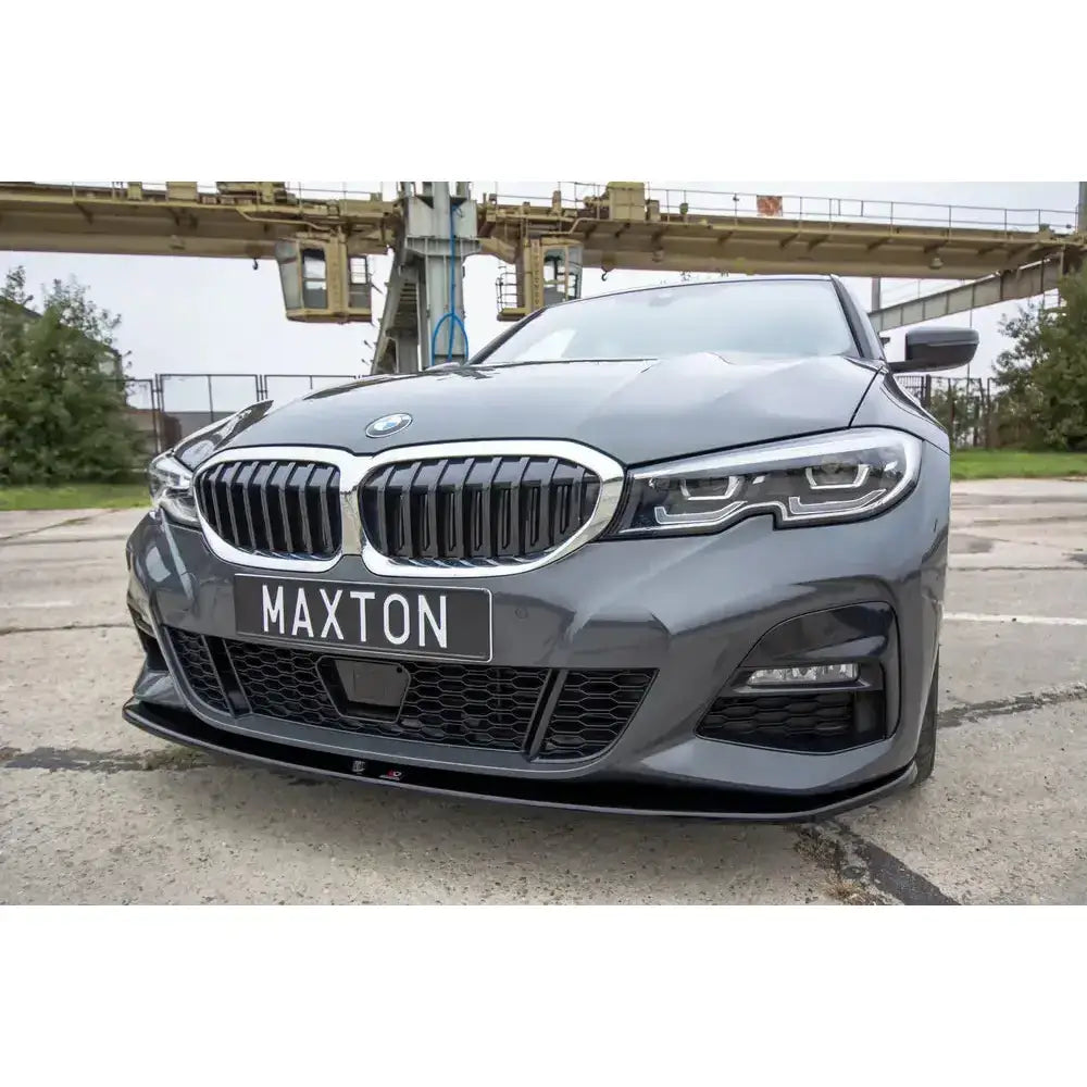 Frontspoiler på BMW 3-serie G20 M-Pack med svart frontsplitter og krom grill mot industriell bakgrunn.