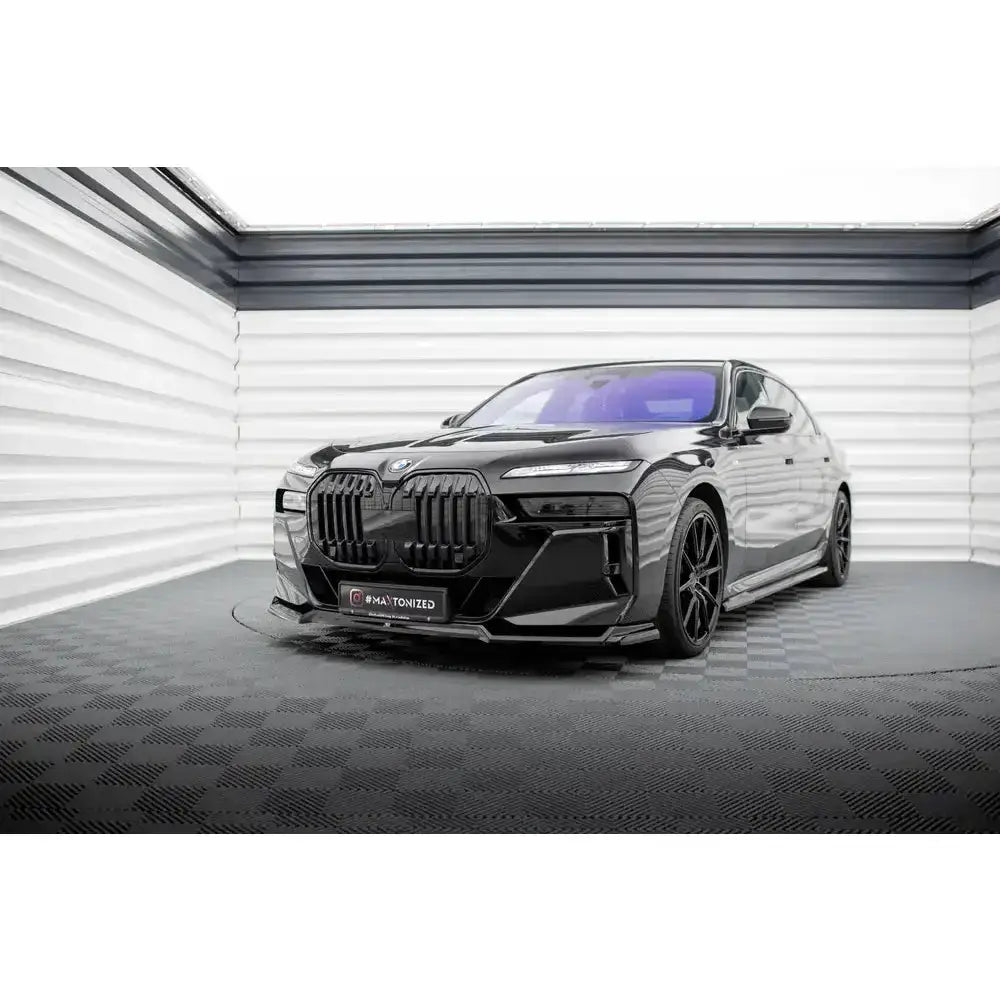 Front lip på BMW 7 M-Pack G70 med sorte felger og stor grill, fotografert forfra i lyst rom.