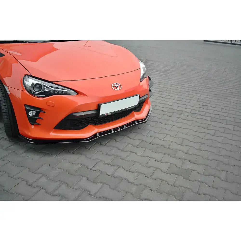 Frontspoiler til Toyota Gt86 Facelift V.3 montert på oransje bil, sett skrått forfra mot belegningsstein.