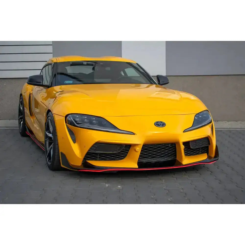 Frontsplitter på gul Toyota Supra Mk5 med svarte detaljer og store luftinntak, parkert på belegningsstein.