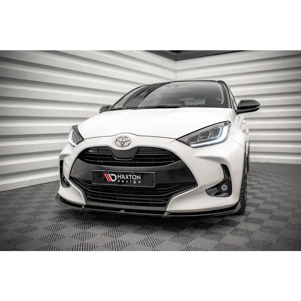 Front lip på Toyota Yaris Mk4 med sort grill, Maxton Design-logo og LED-frontlykter, foran grå stripete bakgrunn.