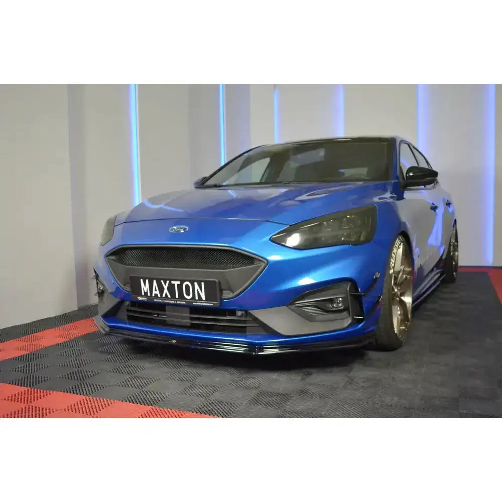 Frontspoiler på blå Ford Focus ST med gullfelger og sportsdetaljer, sett forfra i skrå vinkel innendørs.