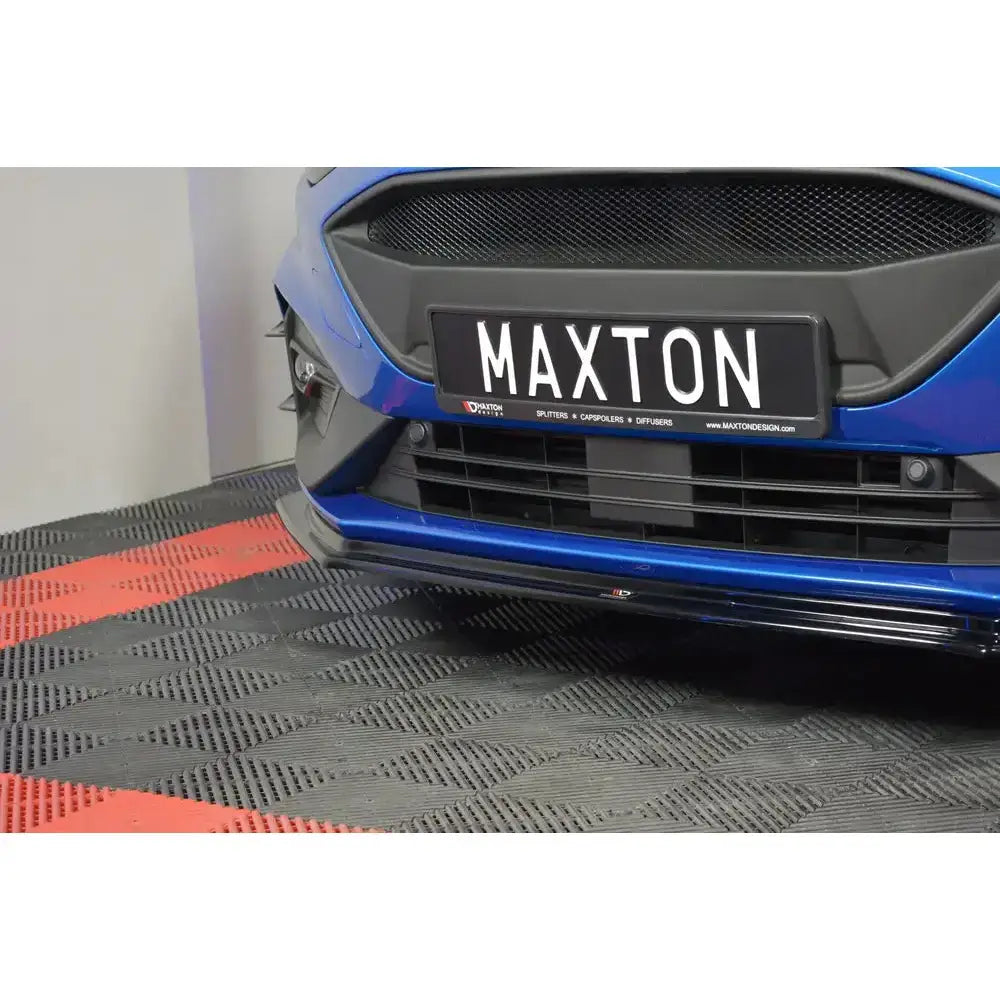 Frontsplitter på blå Ford Focus ST med sort grill, sett forfra på svart og rødt mønstret underlag.