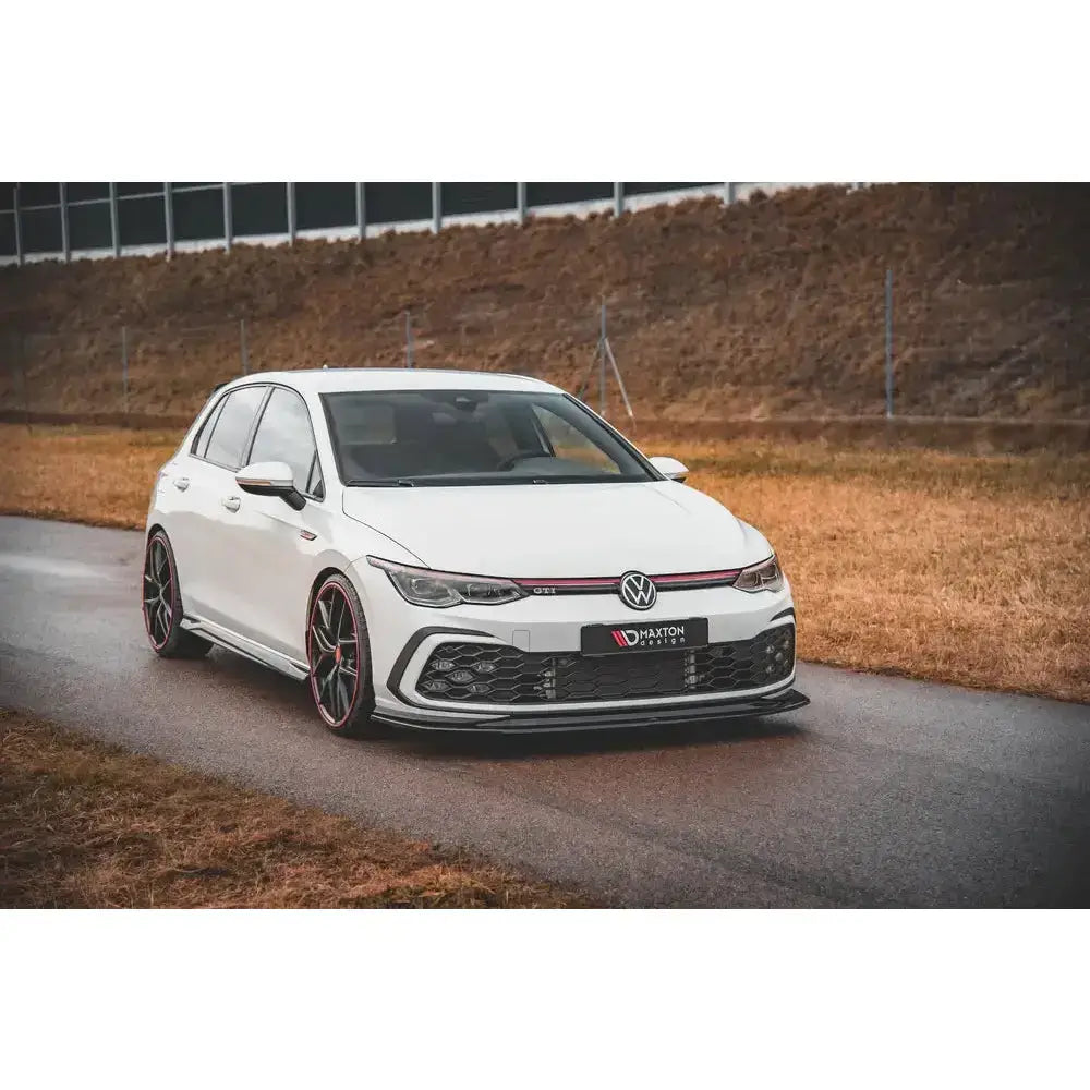 Frontspoiler på Volkswagen Golf 8 GTI V.5, hvit bil med sorte og røde detaljer på våt asfaltvei.