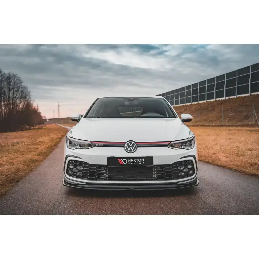 Front lip på Volkswagen Golf 8 GTI V.5, hvit bil med rød stripe og sort frontspoiler utendørs.