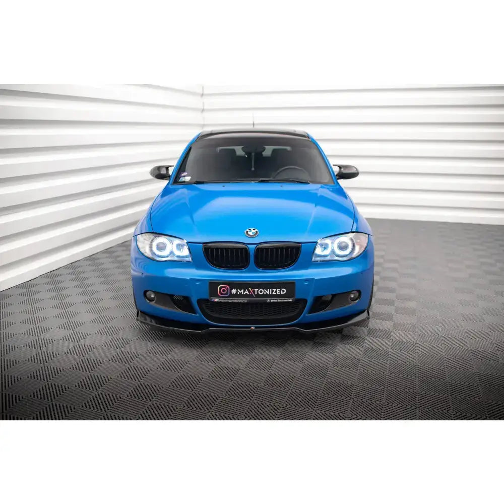 Frontspoiler på blå BMW 1 M-Pack E87 Facelift sett forfra med svarte detaljer og opplyste frontlykter.