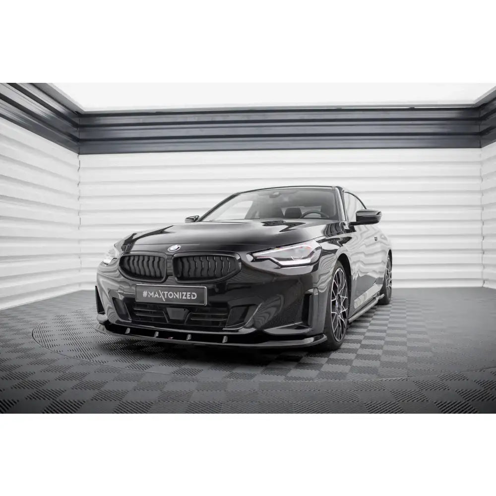Frontspoiler på svart BMW 2 Coupe G42 sett forfra med sportsfelger og mørke detaljer i lyst rom.
