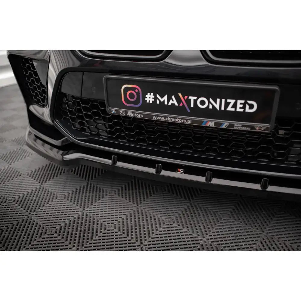 Front lip til BMW X6 M F96 i sort blank plast, sett skrått forfra med detaljer i grill og lykter.