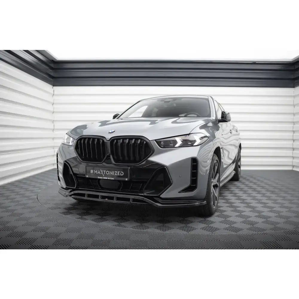 Frontspoiler på BMW X6 M-Pack G06 Facelift med svarte grilldetaljer, sett skrått forfra innendørs.