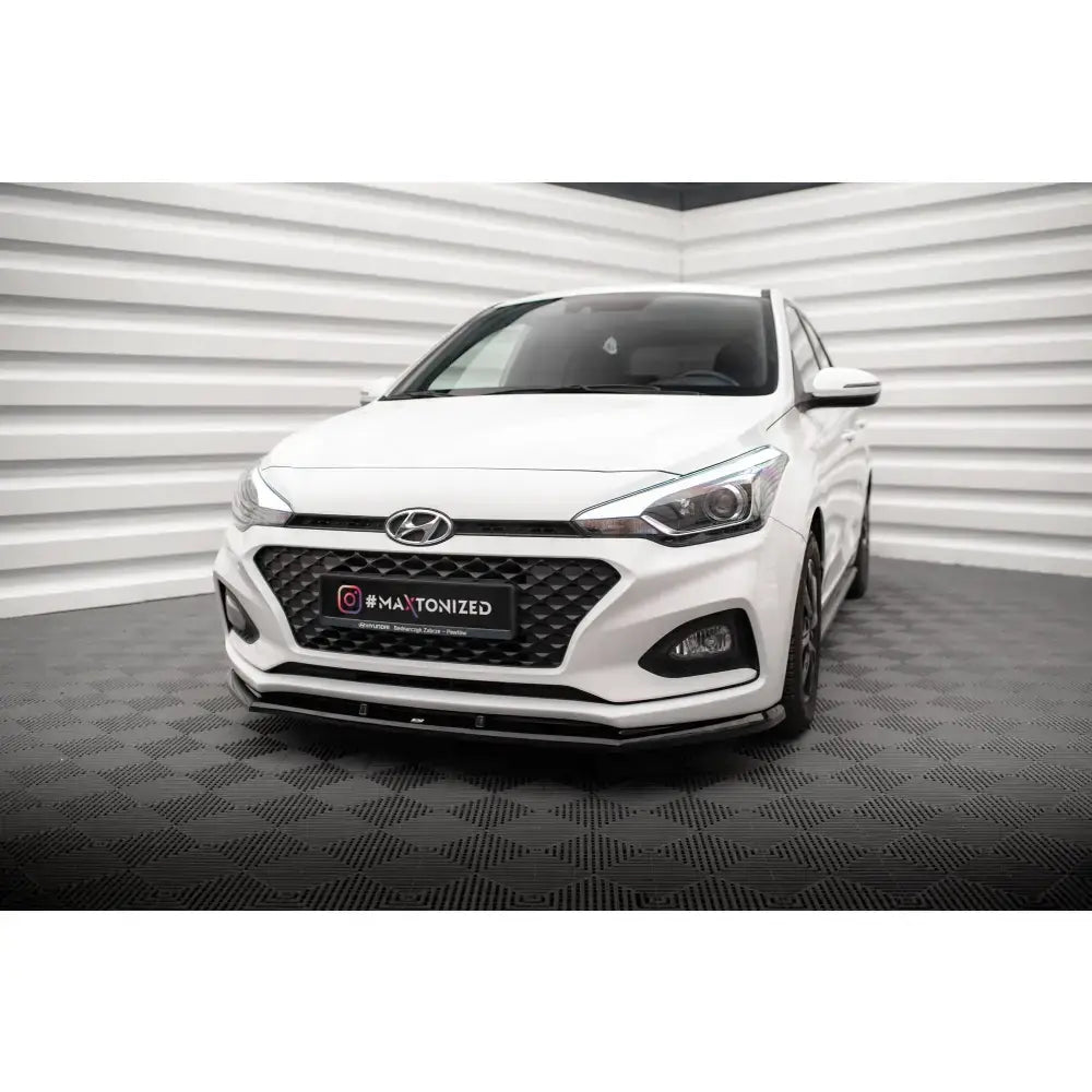 Frontspoiler på hvit Hyundai I20 Mk2 Facelift med svart grill, fotografert innendørs mot bølgete vegger.