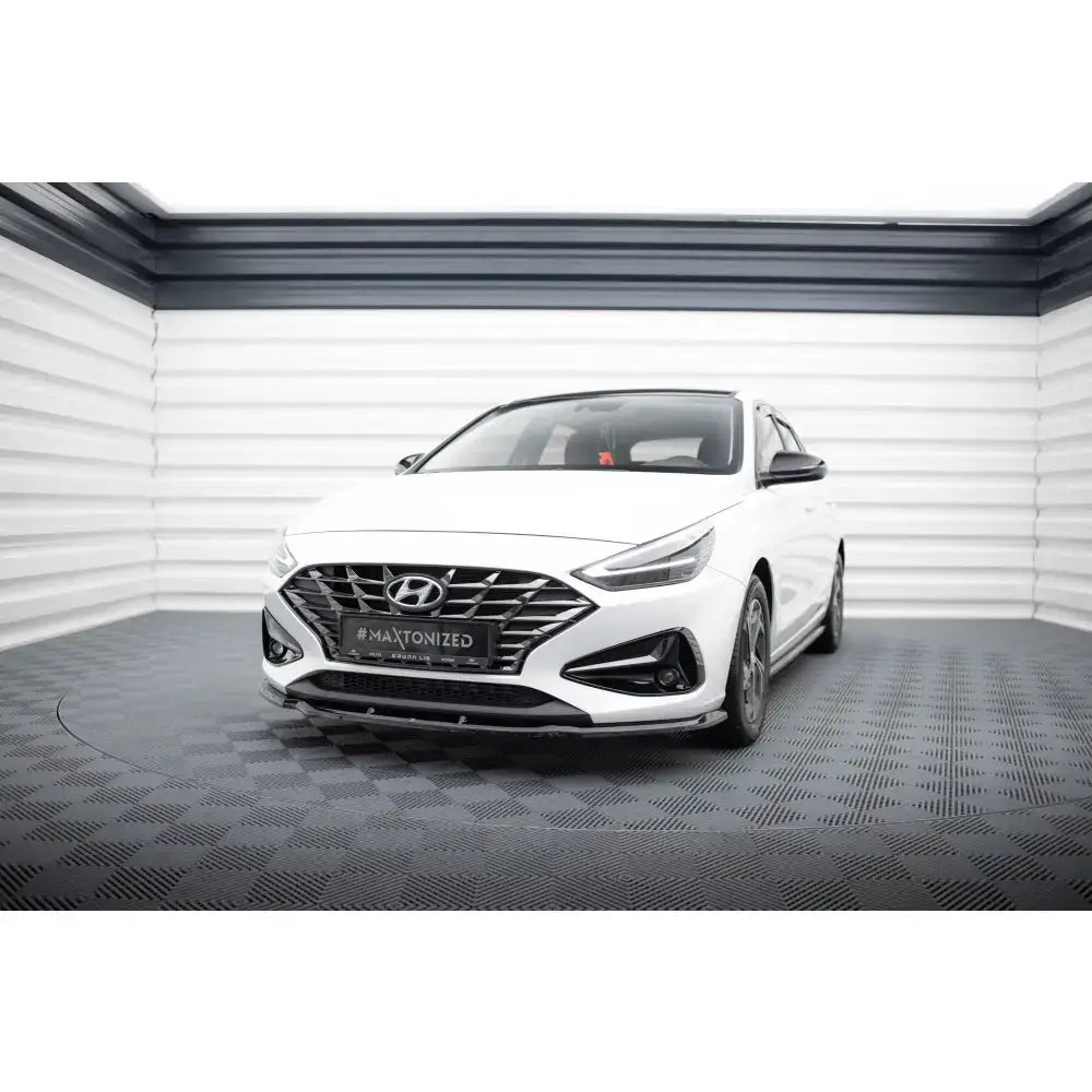 Frontspoiler på hvit Hyundai I30 Mk3 Facelift, sett forfra med mørke detaljer på grill og støtfanger.