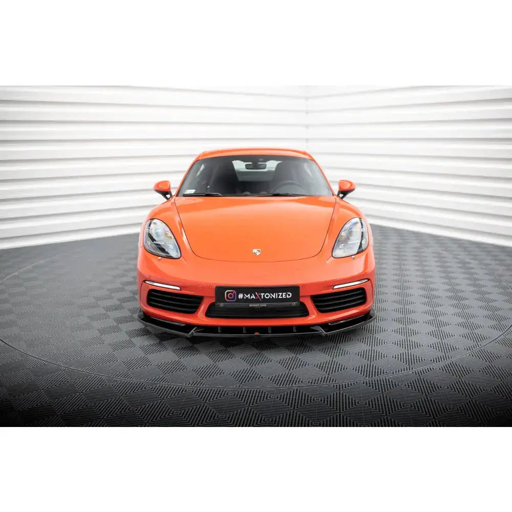 Frontsplitter på oransje Porsche 718 Cayman 982c sett forfra med markante lykter og luftinntak.