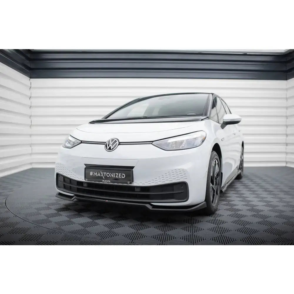 Frontspoiler på Volkswagen ID3 Mk1 hvit bil med sorte detaljer og synlig VW-emblem innendørs.