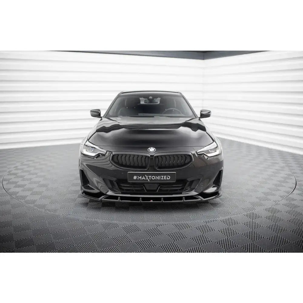 Frontspoiler på BMW 2 Coupe G42 sett forfra med sorte luftinntak og grill, innendørs på mønstret gulv.
