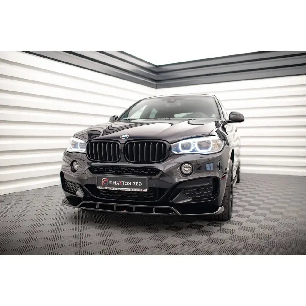 Frontspoiler på svart BMW X6 M-Pack F16 med LED-lys og sort grill i lyst rom med rutet gulv.