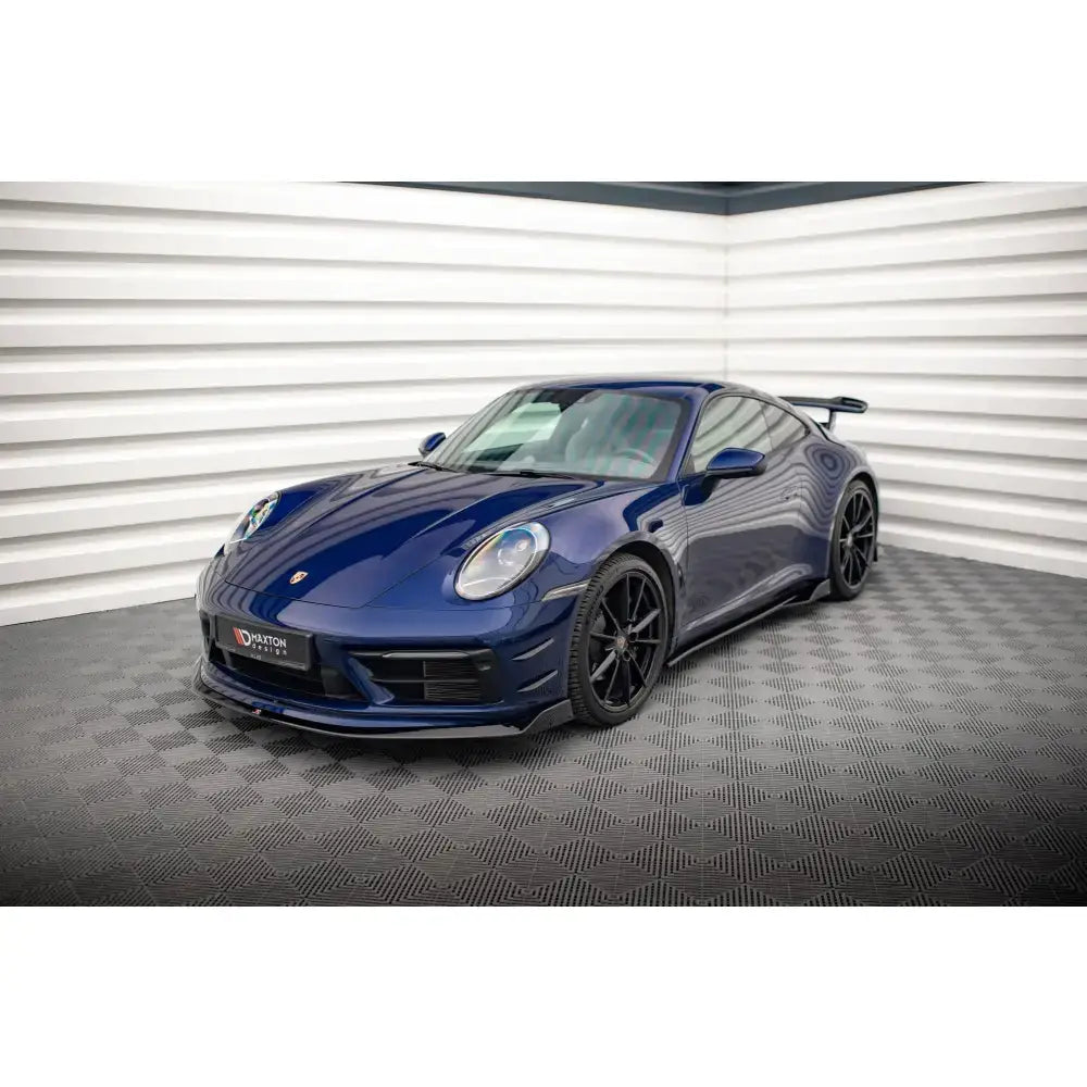 Front lip på blå Porsche 911 Carrera Aero 992 med svarte felger og stor spoiler, innendørs mot hvit vegg.