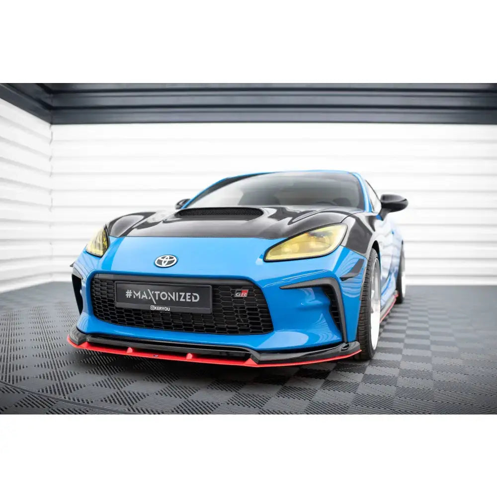 Frontspoiler på Toyota GR86 Mk1 med rød kant, karbonpanser og gule frontlykter, sett skrått forfra.