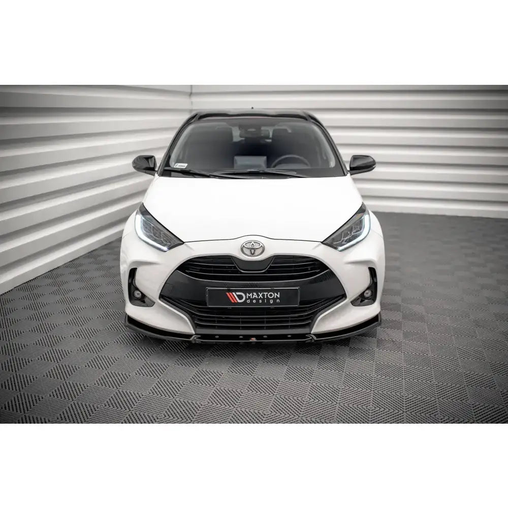 Frontsplitter V2 Toyota Yaris Mk4 på hvit bil med sort grill og Maxton Design-logo, fotografert innendørs.
