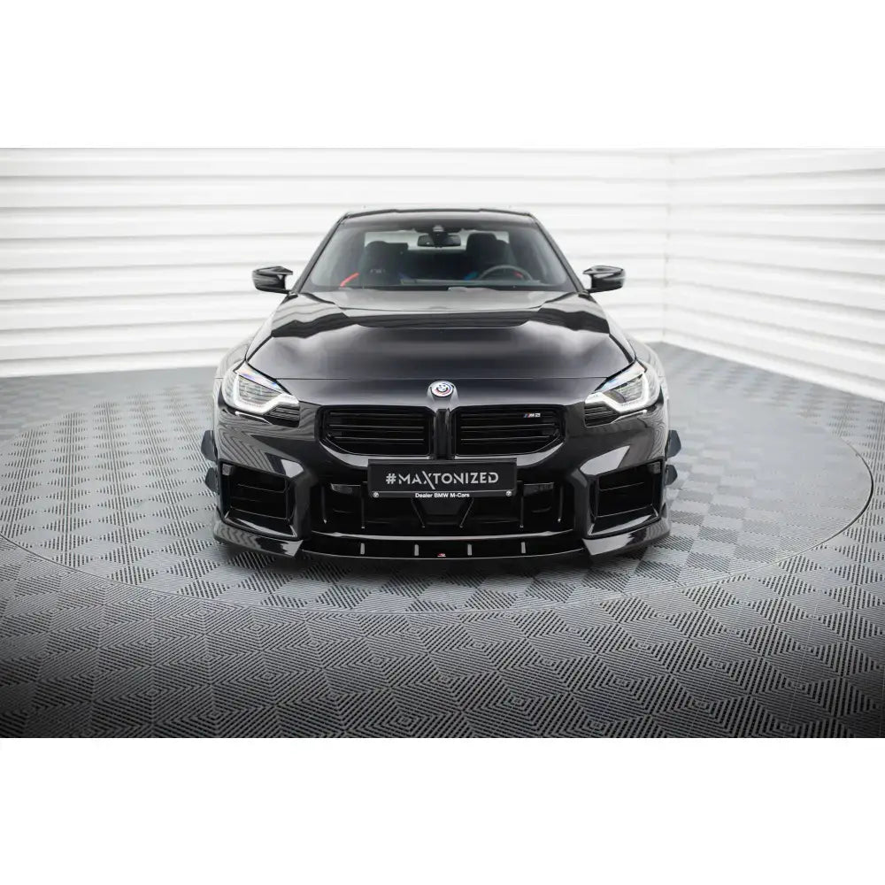 Frontsplitter på BMW M2 G87, sort sportsbil sett forfra med markante luftinntak på grått gulv.