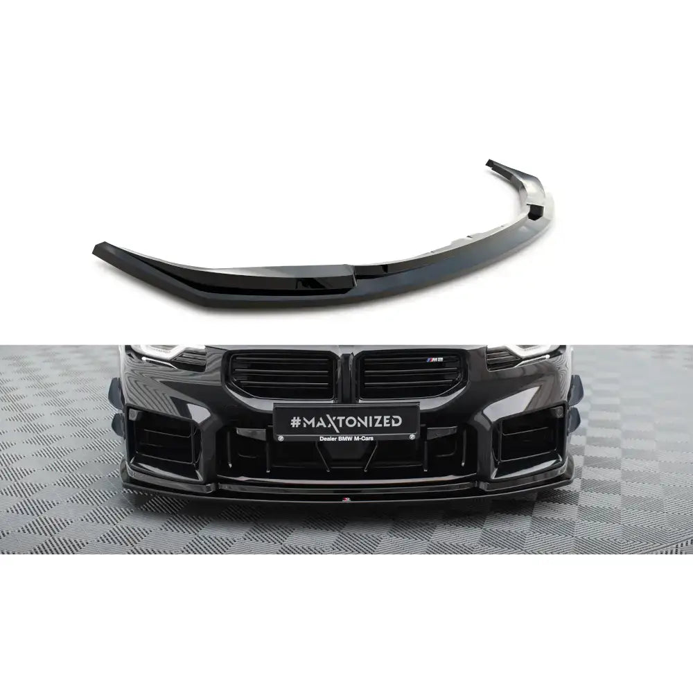 Frontleppe V4 BMW M2 G87 i sort blank plast, vist skrått og montert på bilfront mot rutete gulv.