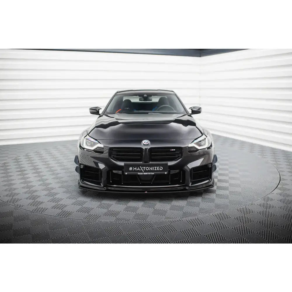 Frontspoiler på sort BMW M2 G87 med markerte luftinntak, sett forfra i lyst fotostudio.