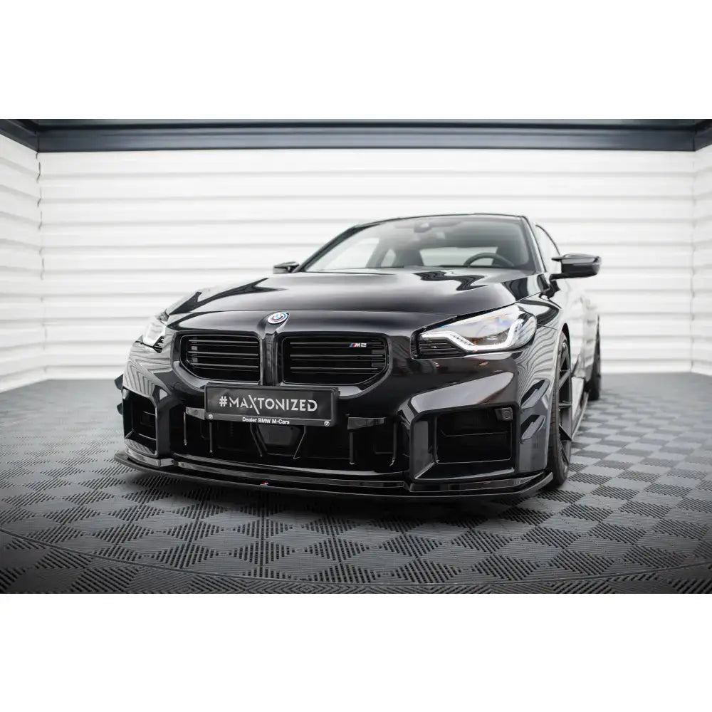 Frontsplitter V4 BMW M2 G87 sett forfra med markant grill og blank sort lakk på rutet gulv.