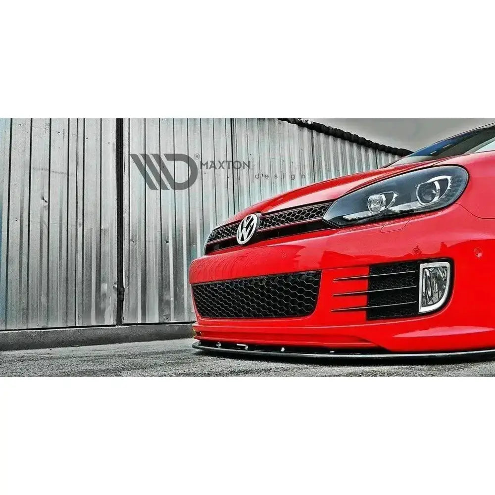 Frontleppe Ver.2 VW Golf VI montert på rød bil med sort grill og frontsplitter foran metallvegg.