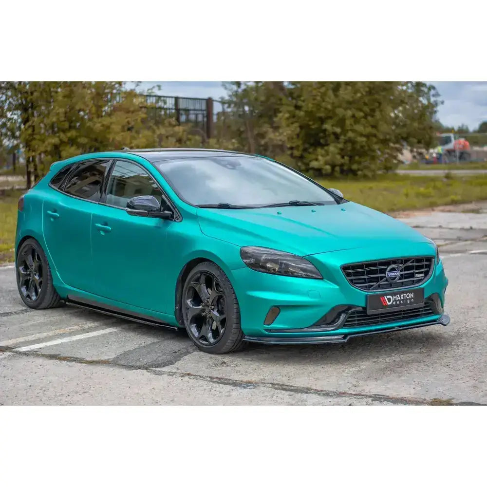 Frontspoiler på Volvo V40 R-Design i turkis metallic med svarte felger, parkert ved grønne busker.