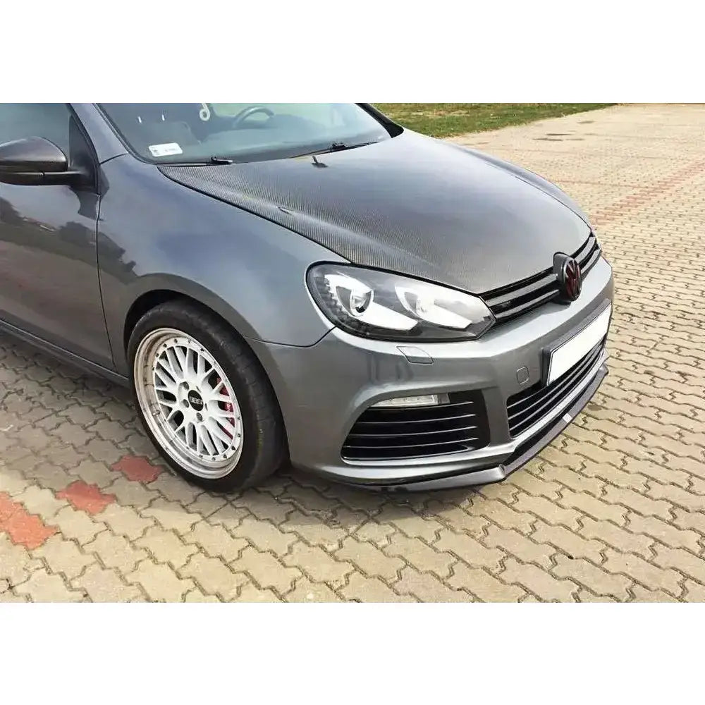 Frontsplitter på Vw Golf VI R med karbonfiberhette, sort grill og ettermarkedshjul parkert på belegningsstein.