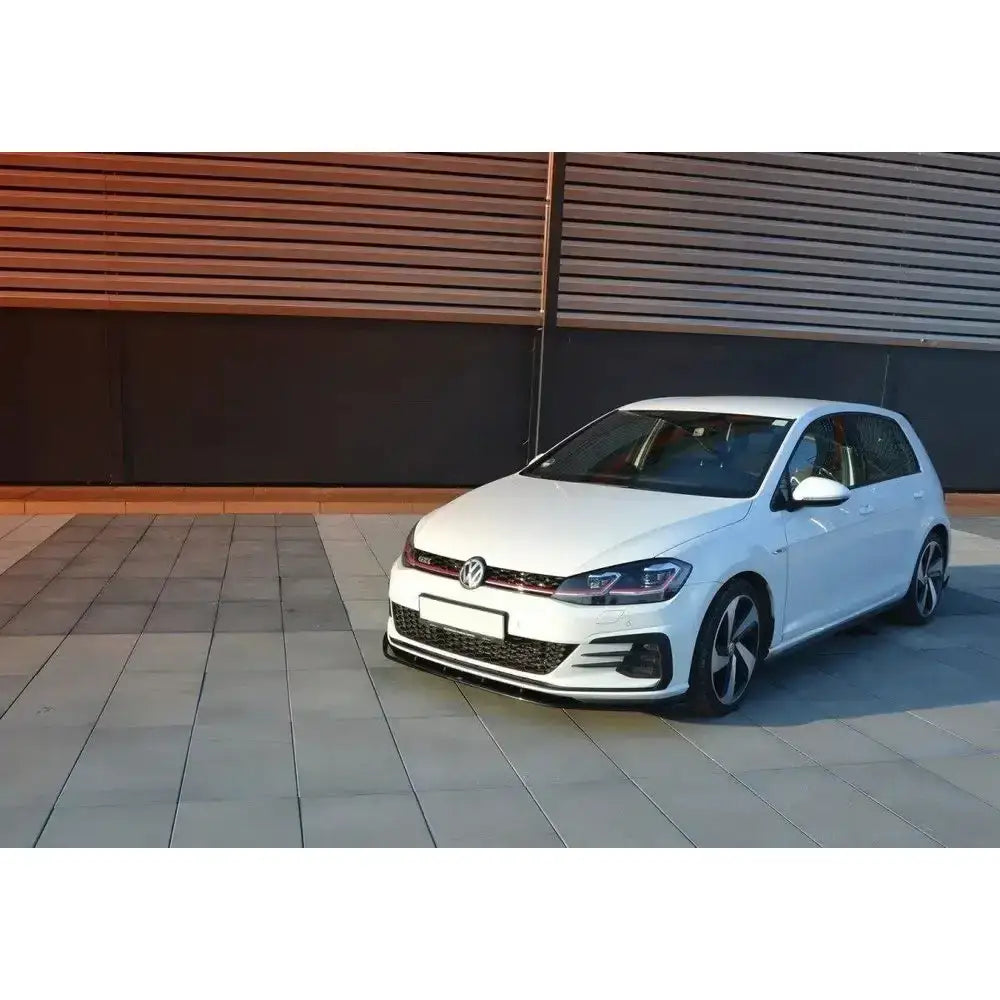 Front lip på hvit VW Golf VII GTI Facelift med sorte og røde detaljer, parkert på steinbelagt plass.