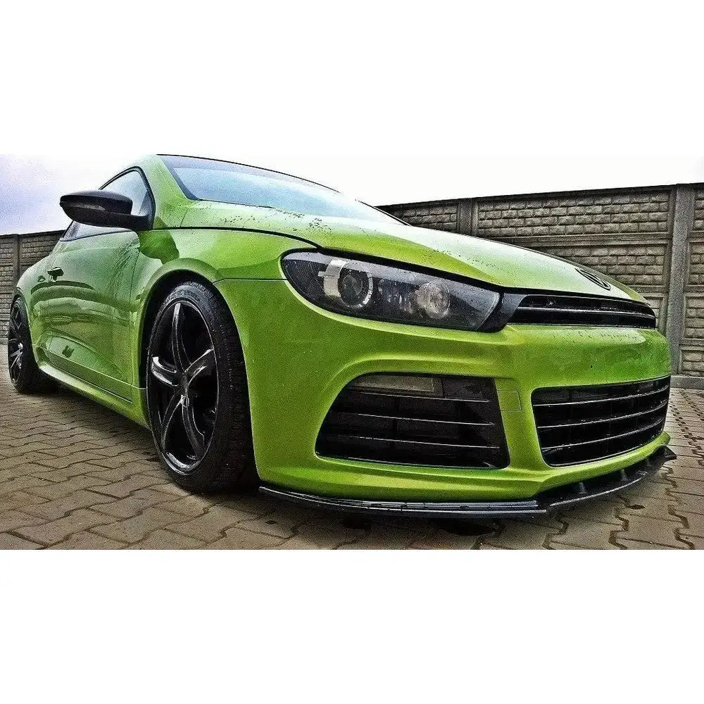 Frontspoiler på grønn Vw Scirocco R med sorte felger, sett forfra på brosteinsbelagt underlag.