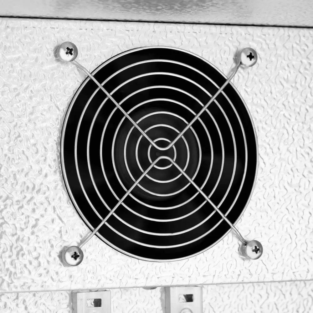 Ventilasjonsvifte med metallgitter på hvit, teksturert overflate fra kjøleskap for drikkevarer.