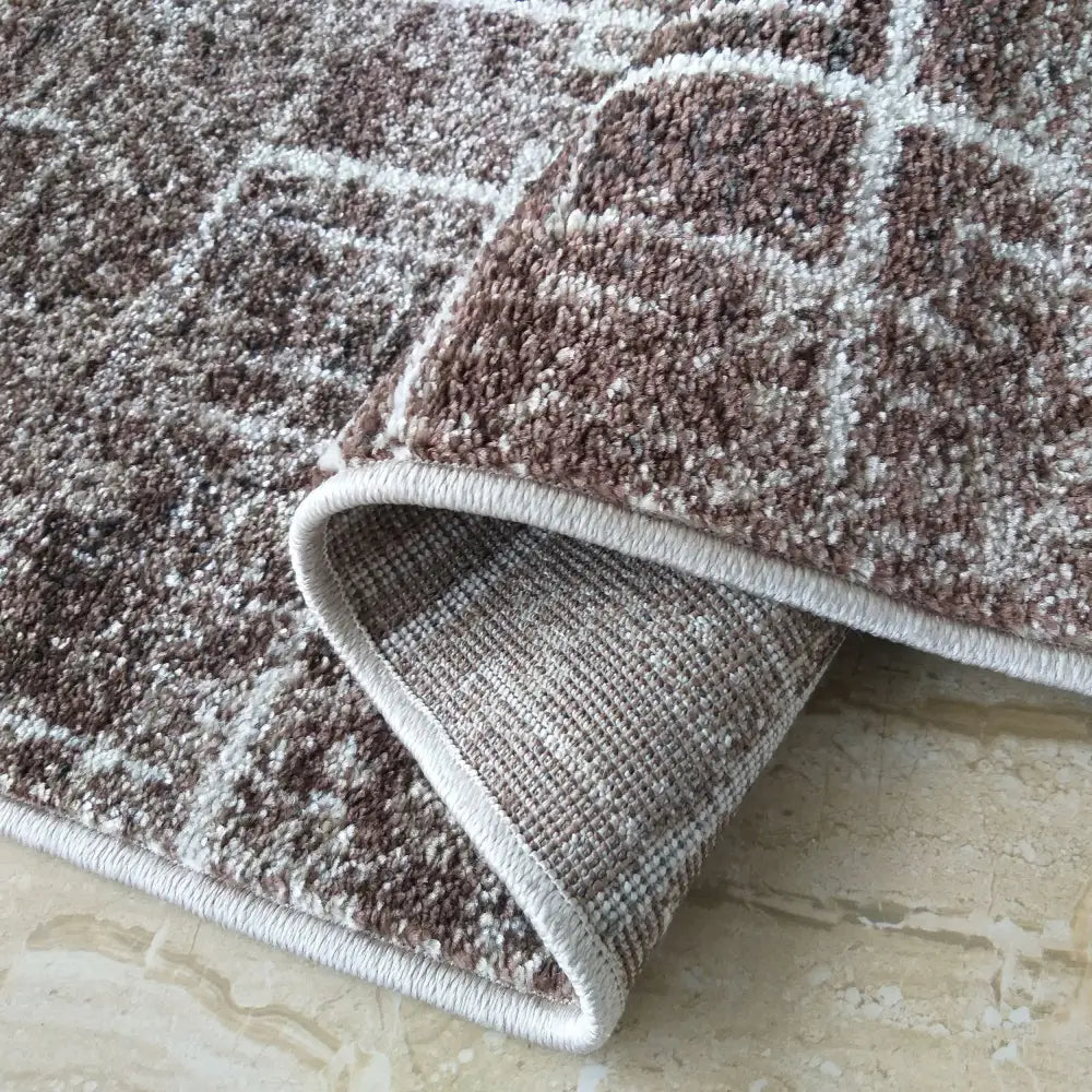 Moderne Panamero teppe i brunt og beige, nærbilde av oppbrettet hjørne som viser tekstur og kant.