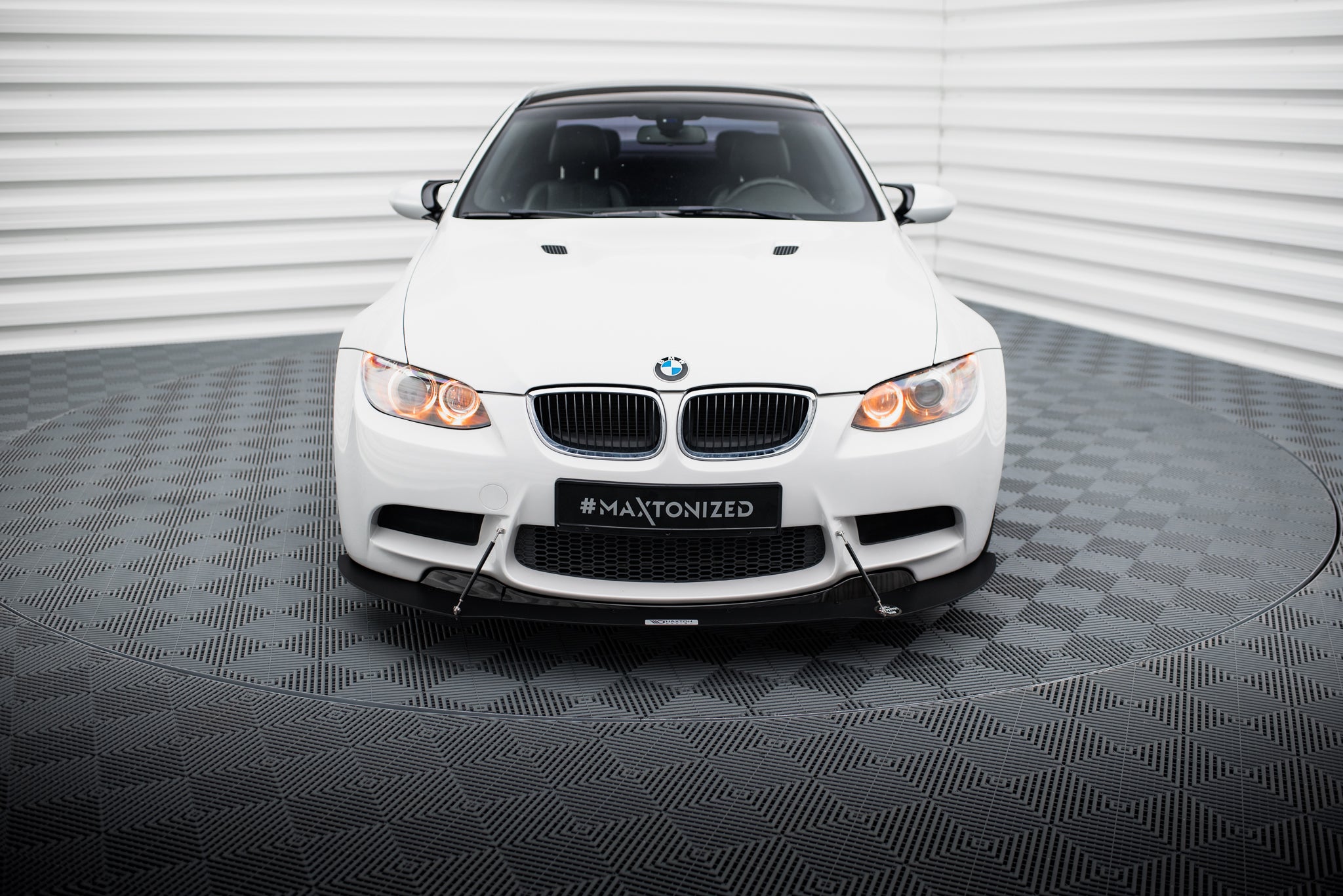 Front splitter på hvit BMW M3 E92 med svarte detaljer, frontlys tent, fotografert rett forfra.