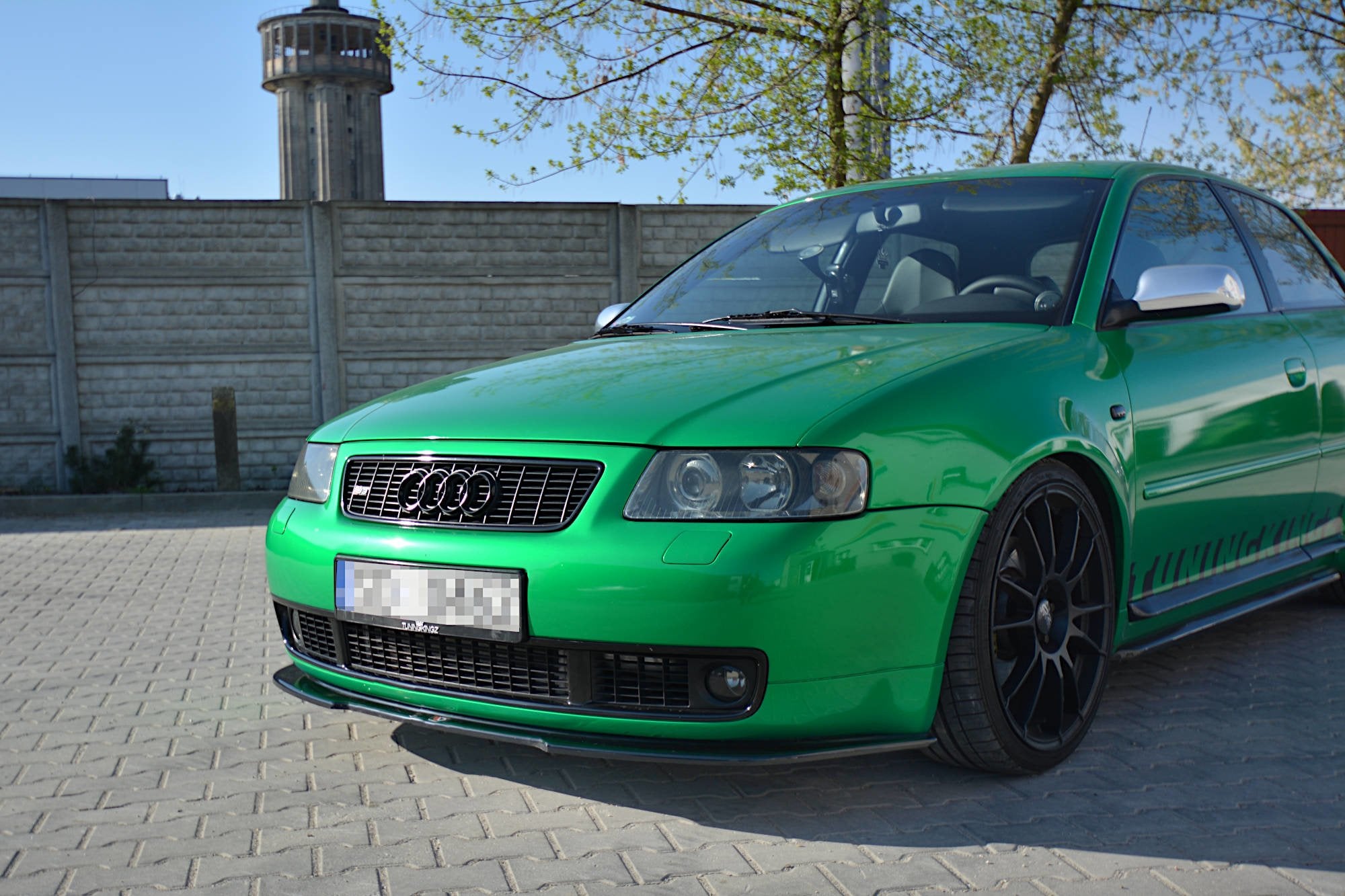 Spoiler Audi S3 8L RS montert på grønn bil med sorte felger og krom sidespeil på brostein.