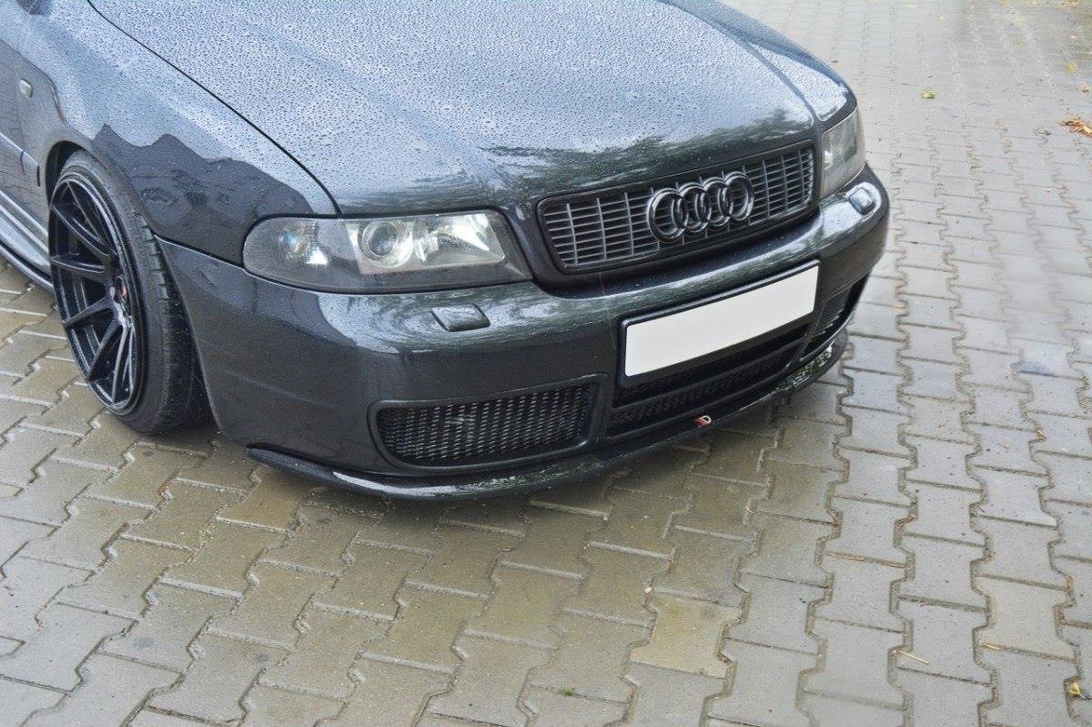 Front splitter på Audi S4 B5, sort bilfront med regndråper, markerte lykter og felg, på brostein.