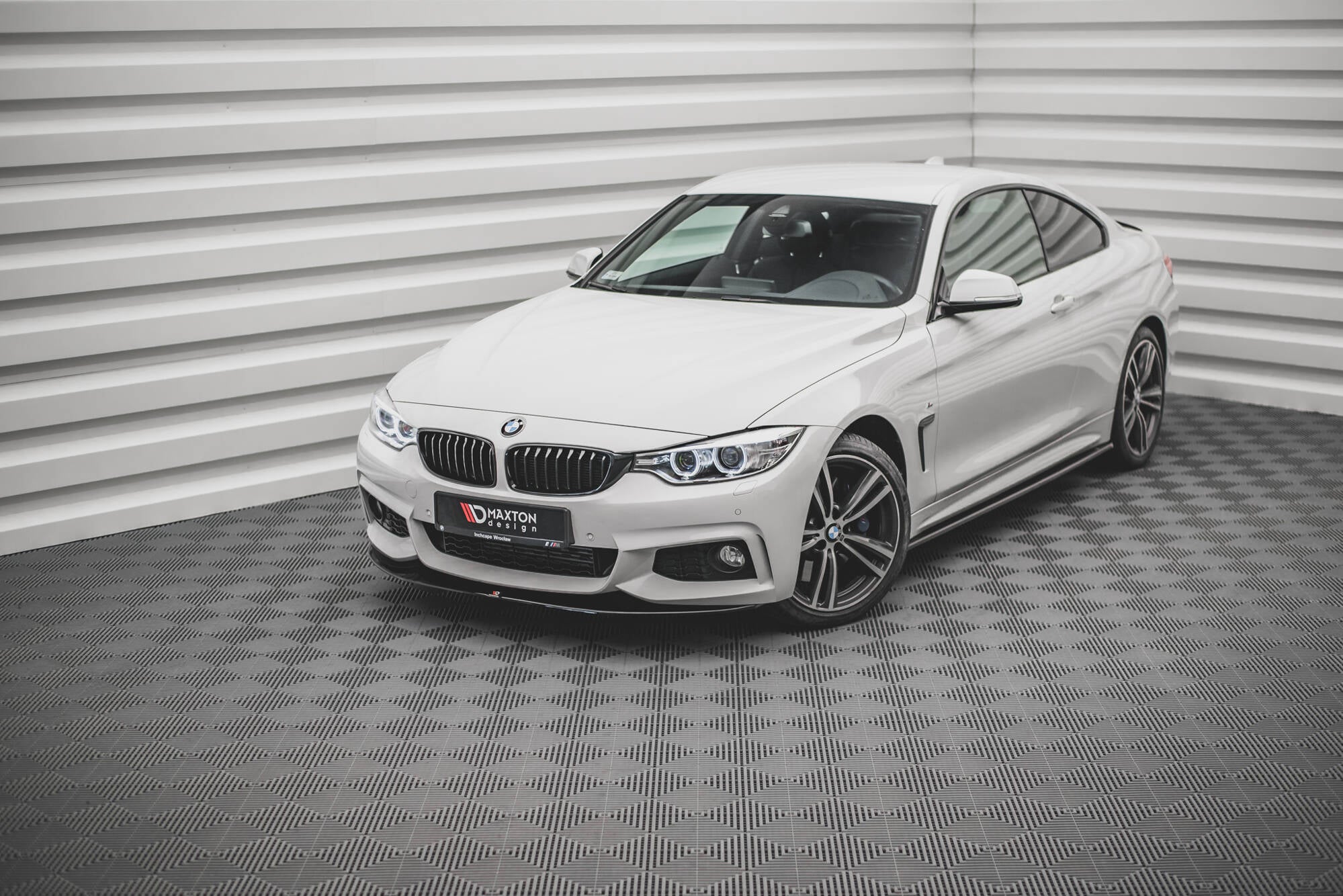 Front lip på hvit BMW 4-serie Coupé med svarte detaljer og store aluminiumsfelger, fotografert skrått forfra.