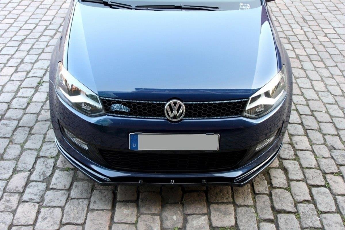 Spoiler på VW Polo MK5, mørkeblå bil sett forfra med grill, frontlys og VW-emblem på brostein.